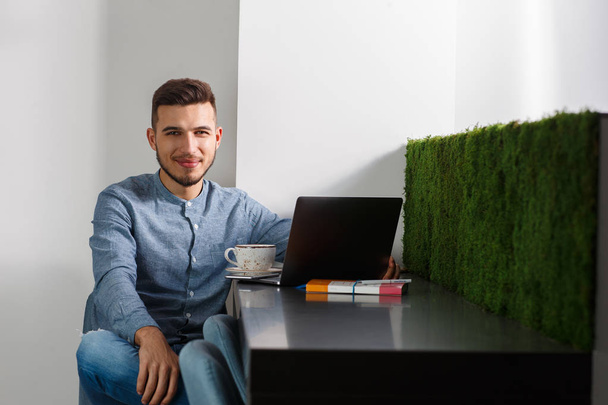 Travailleur indépendant à domicile. Jeune homme souriant en jeans bleu chemise avec ordinateur portable - Photo, image