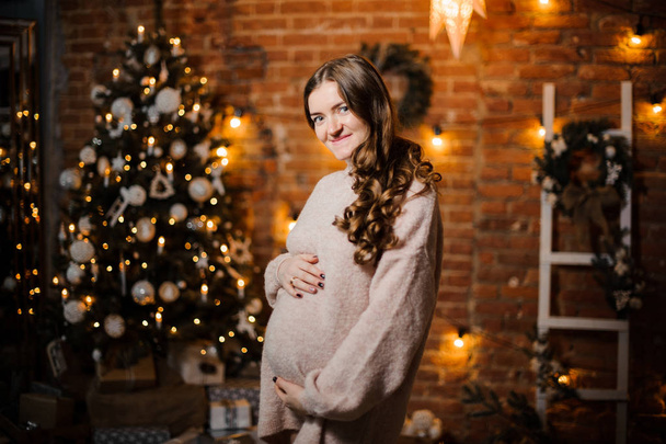 Smiling pregnant woman with long hair against the Christmas tree - Fotografie, Obrázek