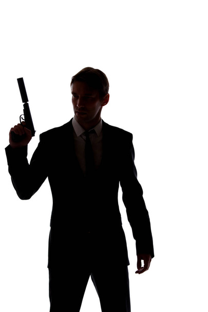 Silhouette of man in business suit with gun at hand isolated on white background - 写真・画像