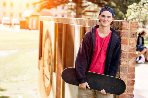 Teenage boy with skateboard standing outdoors - 写真・画像
