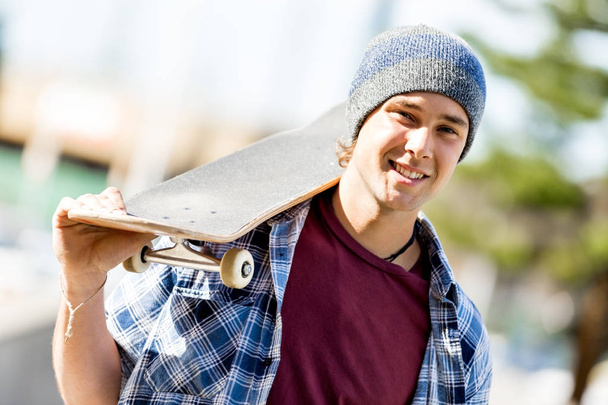 Teenage boy with skateboard standing outdoors - Photo, image