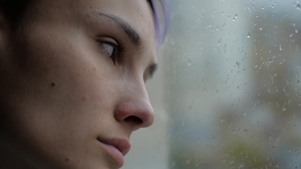 Una mujer triste se sienta y mira por la ventana. Está lloviendo afuera.
 - Metraje, vídeo