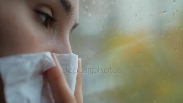 Μια γυναίκα με ένα κρύο τρέχει κοντά σε παράθυρο. Το κορίτσι είναι άρρωστο και sniffs σε χαρτοπετσέτας - Πλάνα, βίντεο