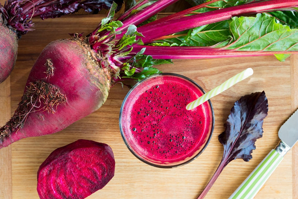 Red beet juice in a glass, with red beets in the background - Photo, Image