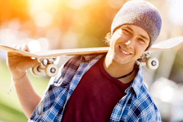 Teenage boy with skateboard standing outdoors - Foto, afbeelding