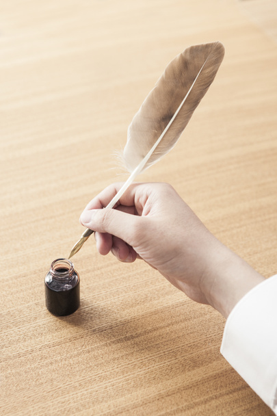 uomo immergendo una penna di piume in una pentola di inchiostro per scrivere una lettera sulla scrivania in legno diurno
. - Foto, immagini