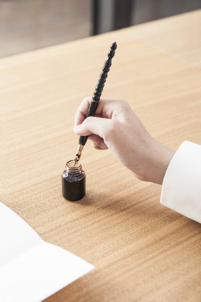 man dipping a pen into an ink pot to write a letter on daylight wood desk. - 写真・画像