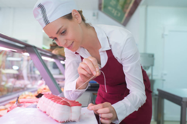 positive female butcher preparing product - Foto, afbeelding
