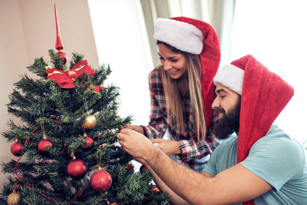 Νεαρό ζευγάρι διακόσμησης ενός χριστουγεννιάτικου δέντρου - Φωτογραφία, εικόνα