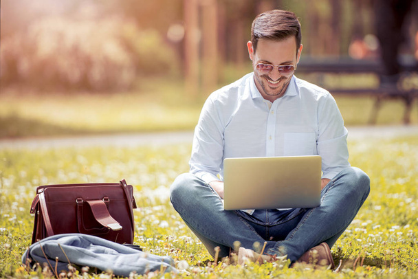 Young man with a laptop sitting on the grass - Φωτογραφία, εικόνα