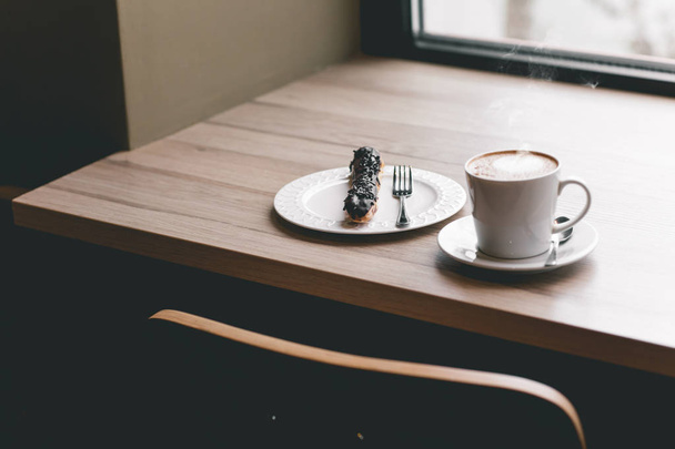 Cup of coffee on wooden table with eclair - Foto, Imagem