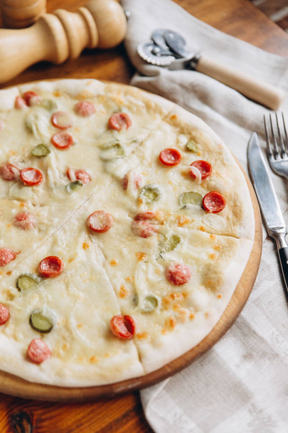 läheinen näkymä maukasta pizzaa salami ja kurkut puinen juoksuhauta liinavaatteet ja hopeaesineet
 - Valokuva, kuva
