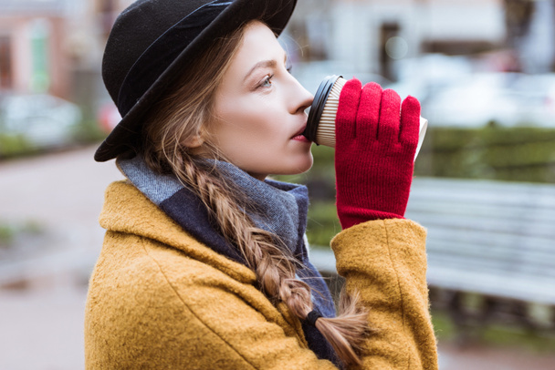 beautiful woman in autumn outfit drinking coffee on bench - Photo, Image