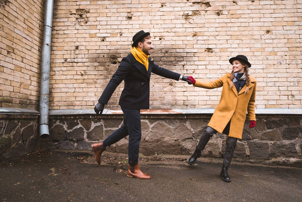 cute young couple holding hands and running beside old building - Photo, Image