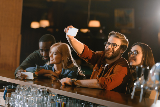 company of attractive young friends taking selfie at bar - Photo, Image