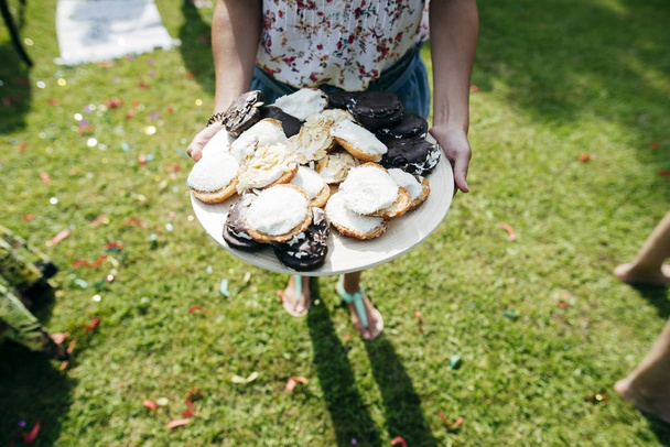 Hochwinkelblick auf weibliches Tablett mit Donuts auf sonnigem Hof - Foto, Bild