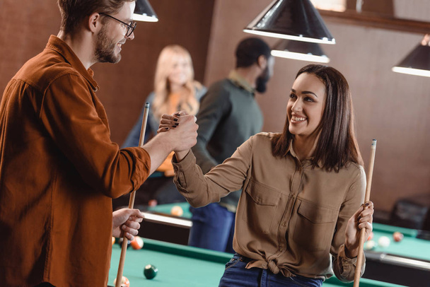 νεαρός ελκυστικός άνδρας και γυναίκα κρατώντας τα χέρια στο pool bar με τους φίλους σας - Φωτογραφία, εικόνα