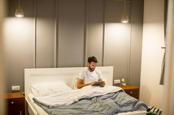 Jeune homme utilisant une tablette numérique couchée sur le lit
 - Photo, image
