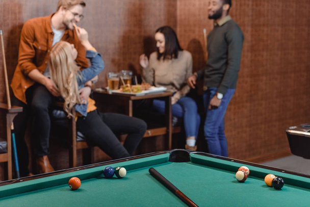 company of multiethnic friends eating and drinking beside pool table at bar  - Foto, Imagem