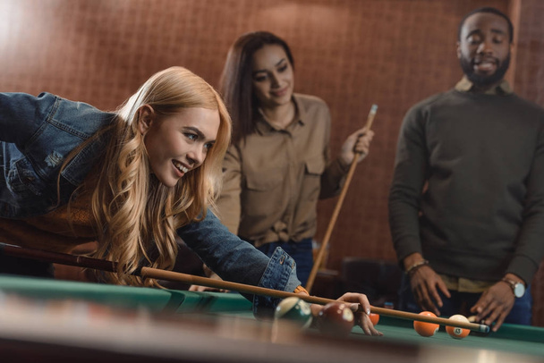 молодые успешные многонациональные друзья играют в бильярд в баре
 - Фото, изображение