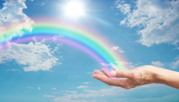 He aquí un hermoso arco iris para usted mano femenina con un arco iris brillante a través de un cielo azul con nubes esponjosas y un sol brillante estalló
 - Foto, imagen