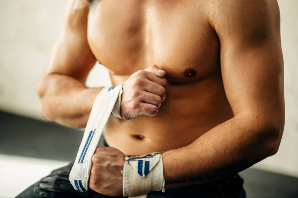 Muscular weightlifter wrapping hands and preparing for workout at a gym. - Valokuva, kuva