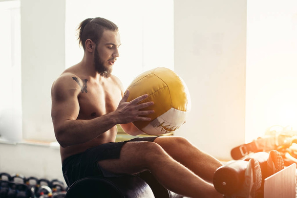 man doing sit ups with medicine ball on bench, working on abdominal muscles - Foto, afbeelding