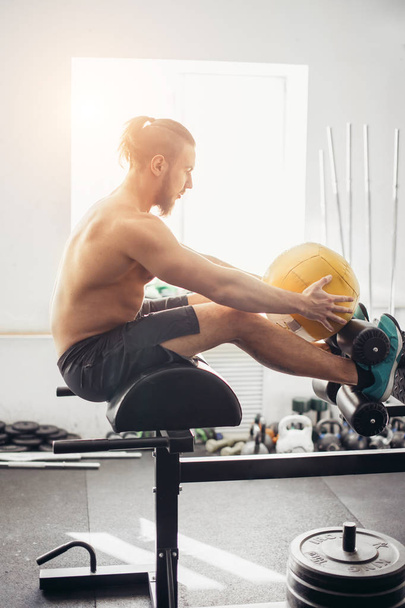 man doing sit ups with medicine ball on bench, working on abdominal muscles - Fotografie, Obrázek