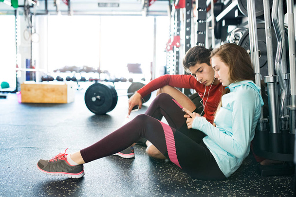 Fit couple in modern crossfit gym with smartphone. - Фото, изображение