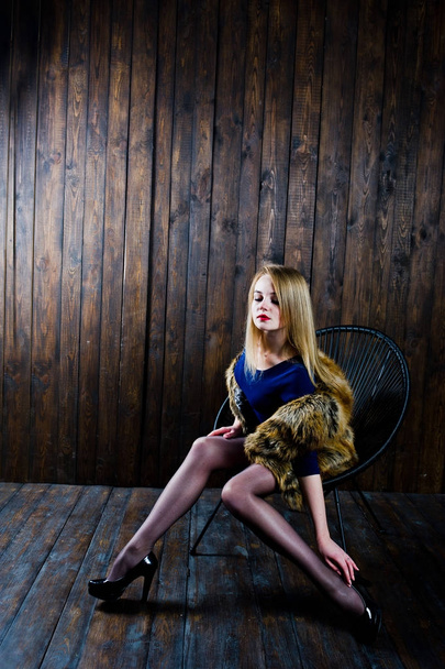 Elegante blonde girl wear on fur coat sitting on chair at studio - Фото, зображення