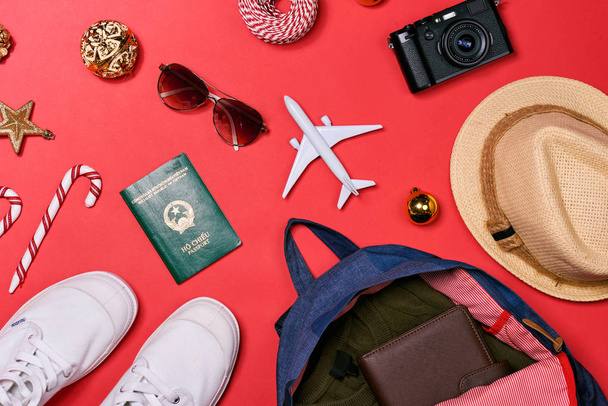 Preparación para el concepto de viaje - pasaporte, cámara, sombrero, avión, adornos de Navidad sobre fondo rojo
 - Foto, Imagen