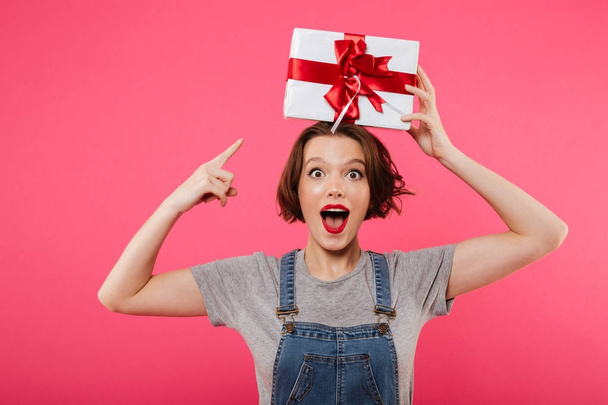 Excited young woman holding gift box pointing. - Foto, imagen