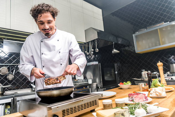 smiling chef frying meat in restaurant kitchen - Foto, Imagem