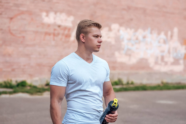 A male athlete goes in for sports in the open air. Muscular arms. Blonde in a white T-shirt. Lifestyle of the bodybuilder - Valokuva, kuva