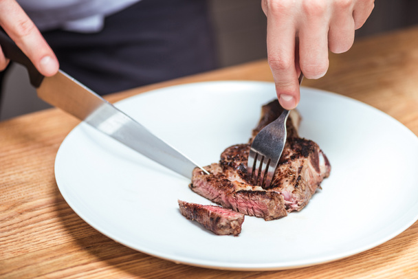 cropped image of chef cutting fried meat with knife and fork  - Foto, Bild