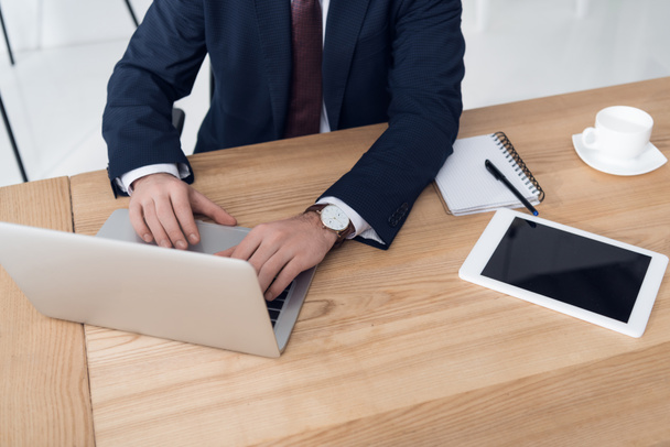 vista parziale di uomo d'affari che lavora su computer portatile a posto di lavoro con targa in ufficio
 - Foto, immagini