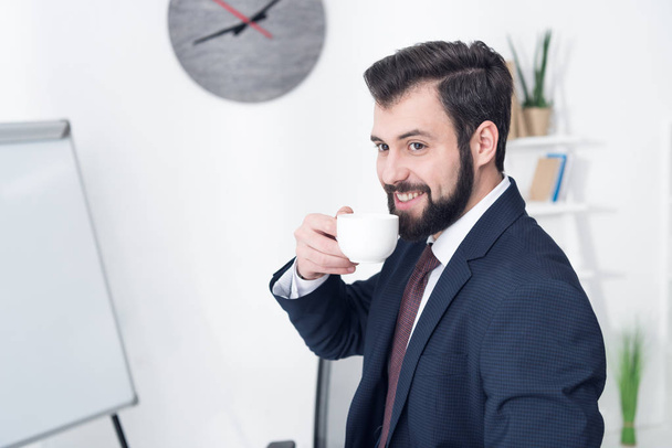portrait of smiling businessman drinking coffee in office - Fotoğraf, Görsel