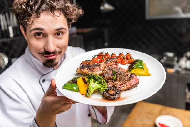chef souriant montrant des légumes cuits avec de la viande sur l'assiette
 - Photo, image