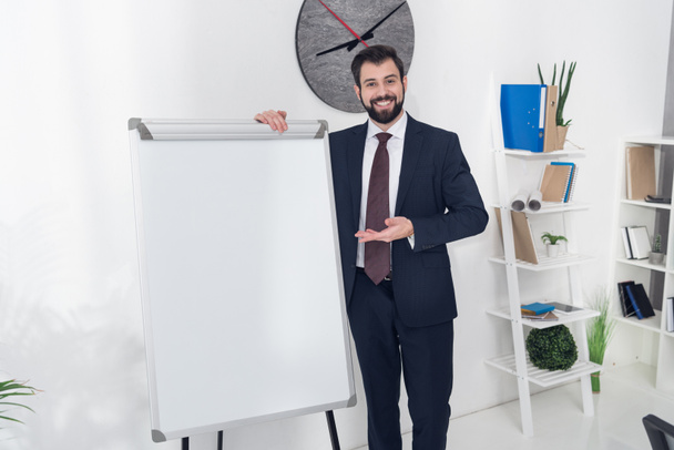 Улыбающийся бизнесмен указывает на пустую белую доску в офисе
 - Фото, изображение