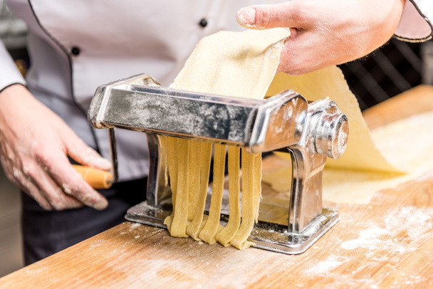 abgeschnittenes Bild vom Koch, der Pasta mit Pasta-Hersteller macht - Foto, Bild