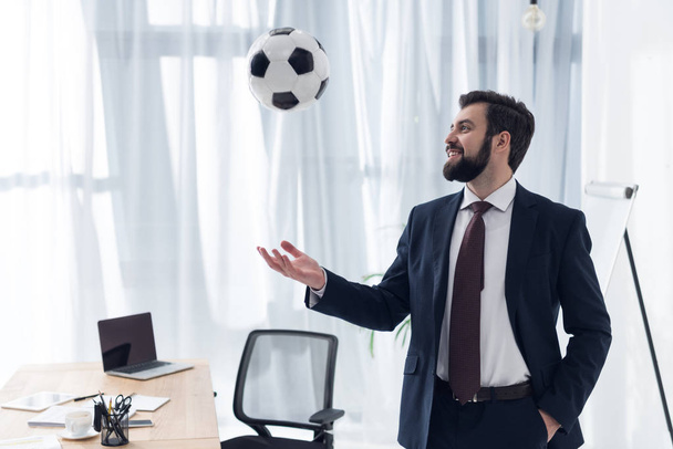 Porträt eines lächelnden Geschäftsmannes, der am Arbeitsplatz im Büro mit Fußball spielt - Foto, Bild
