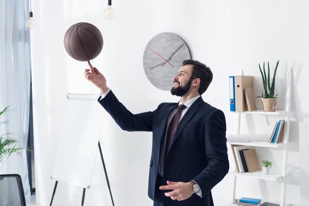 side view of young businessman in suit playing basketball in office - Фото, изображение