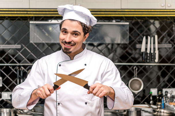 smiling chef standing with crossed knifes - Zdjęcie, obraz