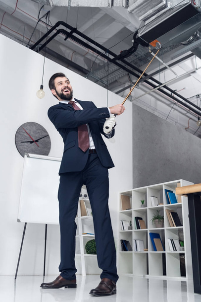 low angle view of smiling businessman in suit playing golf in office - Foto, Imagem