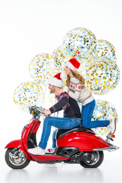 весела пара в капелюхах Санти їде на червоному скутері, великі різдвяні кульки з конфетті на фоні, ізольовані на білому
  - Фото, зображення