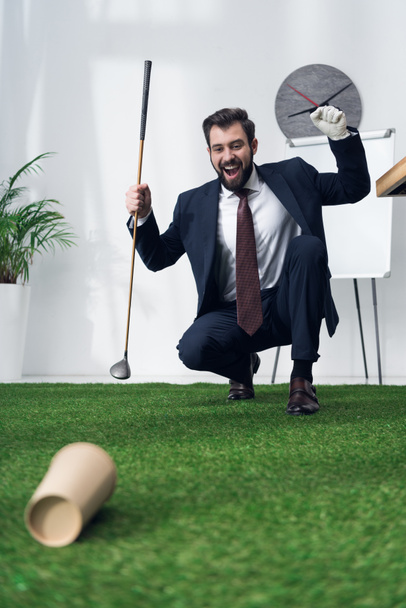 aufgeregter junger Geschäftsmann spielt Golf im Büro - Foto, Bild