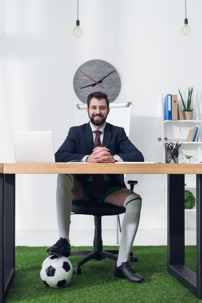 sonriente hombre de negocios con pelota de fútbol sentado en el lugar de trabajo en la oficina
 - Foto, imagen