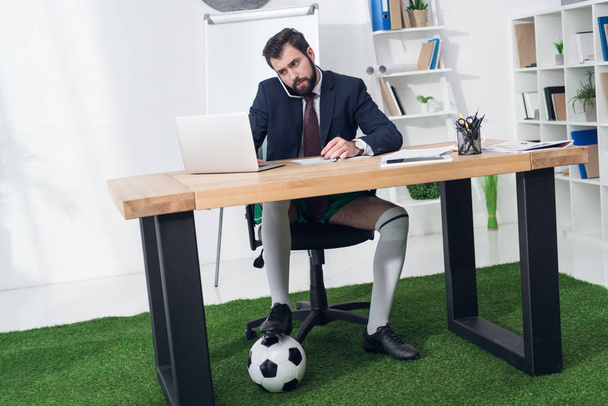 Geschäftsmann mit Fußballball spricht am Arbeitsplatz im Büro auf dem Smartphone - Foto, Bild