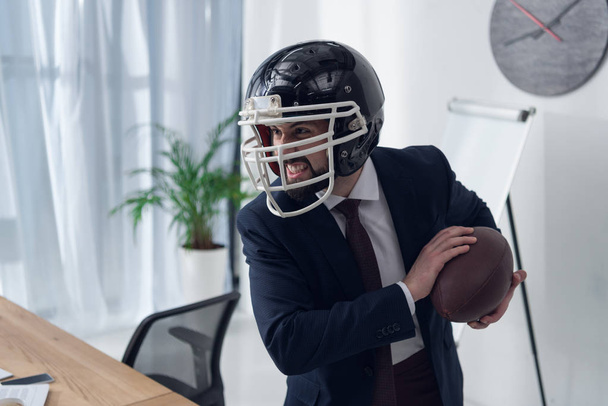 joven hombre de negocios furioso en casco jugando rugby en la oficina
 - Foto, Imagen