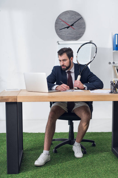 gericht zakenman met tennisracket werken bij werkplek op kantoor - Foto, afbeelding
